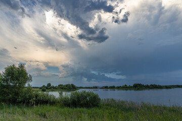 Dramatic Sky Horizon Summer Landscape Rain Clouds Lake Bright green on the shore of the reservoir, after the rain. Large thundercloud.