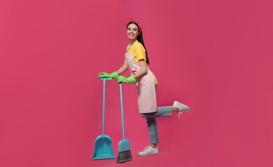 Fototapeta premium Young housewife with broom and scoop on pink background