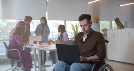 Disabled young man in wheelchair working in on laptop in modern office