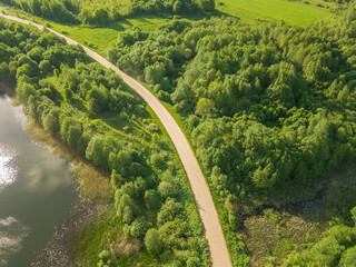 Winding road along the lake on a sunny summer day, view from a drone. Beautiful landscape from drone to fields, lakes, forests, village