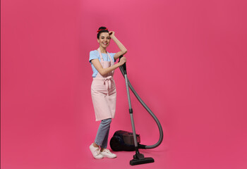 Housewife with vacuum cleaner on pink background