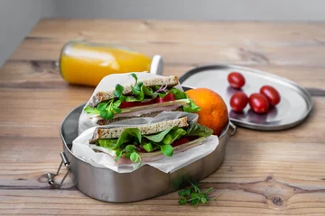 Fototapeten Sandwich mit Salatblätter und Schinken in einer wiederverwendbaren Blechdose, Orangensaft und Cocktailtomaten auf einem Holz Tisch. © Sonja Rachbauer
