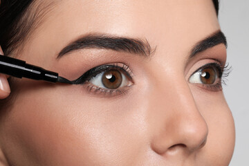 Artist applying black eyeliner onto woman's face on grey background, closeup - obrazy, fototapety, plakaty