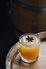 autumnal apple cider cocktail with star anise garnish on wooden whiskey barrel with dark background