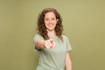 Portrait defocused young redhead girl with curly hair smiling looking at camera pointing fingers with green t-shirt on green background