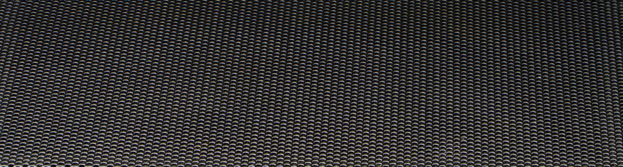 Steel black metal mesh with many small circular holes, close-up view. Abstract horizontal photo with an industrial pattern.