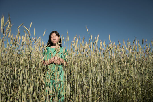 asian girl in green dress standing in the middel of a wheat grain field under blue sky in summer
