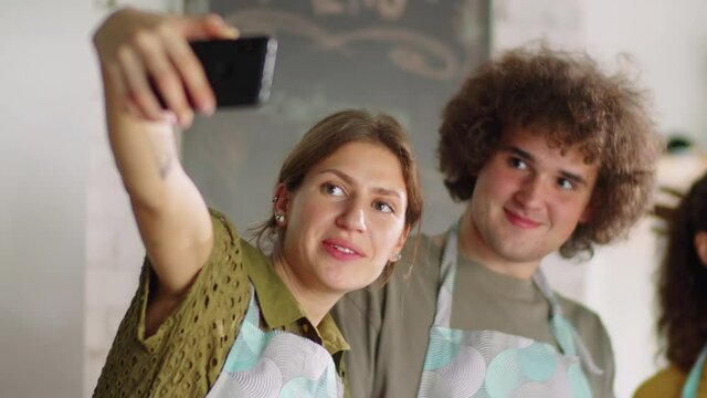 Group of cheerful multiethnic men and women holding dishes and posing for smartphone camera with smile while taking selfie during cooking master class