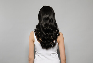 Young woman with long curly hair on grey background, back view