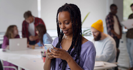 Smiling afro-american businesswoman using phone in modern busy office.