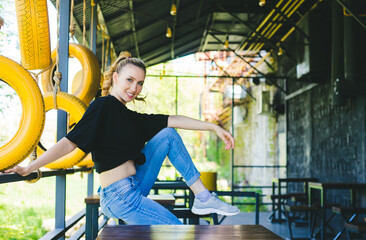 A young athletic woman sits in a relaxed position on a chair in a cafe. Summer terrace or veranda.