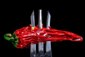 a single dried chili pepper on a fork shot against a black background, macro, close up shot