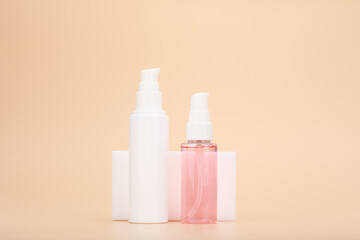 Cosmetic set with face cream or lotion and pink cleansing foam in transparent bottle with dispenser on bright beige background. Concept of beauty products for daily skin care