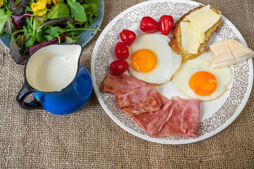 Breakfast table with egg,tomato,bread, cheese, salad and blue pitcher on jute.