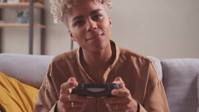 Young excited concentrated African American female player sit on couch at home alone game player with joystick in hand playing console games. Gaming free time on weekend funny activity concept