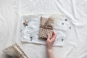 Hand hold gift wrapped in beige craft paper with dry wild grass tied up with cotton cord. Flat lay...