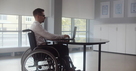 Positive disabled young man in wheelchair working in office