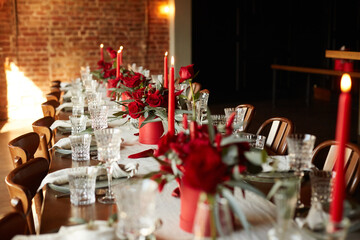 Unusual decoration of a wedding table with red roses, eucalyptus in red boxes with red candles and chili peppers in a dark interior