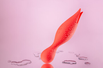 Orange vaginal dildo with vibration on a pink background. Clitoral vibrator located on the mirror. Sex toy covered with drops. Space for text. Image for the sex shop. Toys for adult.