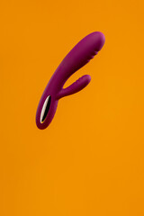 Purple dildo in the air. Vaginal and clitoral vibrator on a yellow background. Sex toy. Sex shop. View from above. Advertising concept. Sex gadget and masturbation device. Place for text