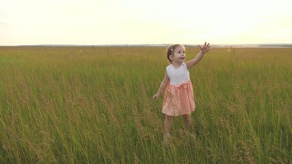 Naklejka na ściany i meble Child, girl playing in summer in park laughs and claps. A happy family. Happy little girl runs across field with green grass in spring, childhood dreams and fantasies. Cheerful kid runs on green grass