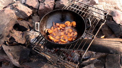 Fried shrimp in a cauldron over a fire.