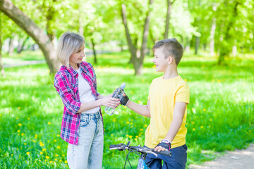 Mother giver bottle of water to young boy while riding a bicycle. Mom cares about her son's health...