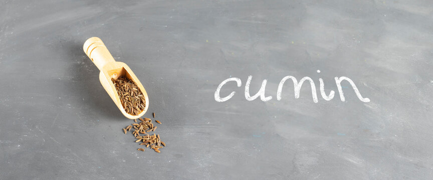 Cumin seeds in a wooden spoon on a gray background with the inscription in chalk