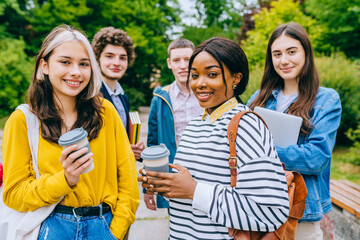 Fototapeta premium Multi-ethnic group of five students friends spending time together outdoors at college campus, chatting, discussing classes schedule. Education and friendship concept.