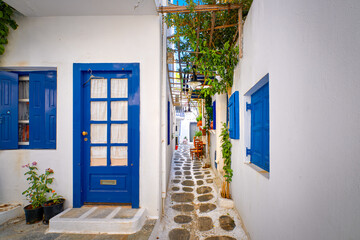 Beautiful traditional narrow alleyways of Greek island towns. White houses, flower pots, blue windows and doors. Mykonos, Greece