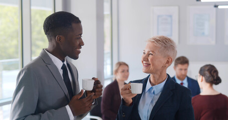 Interracial business colleagues drinking coffee while talking in office