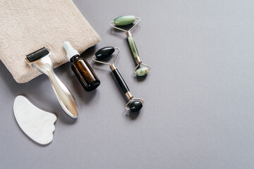 Skincare tools: microneedling derma roller, jade guasha massage rollers and serum bottle on the gray background