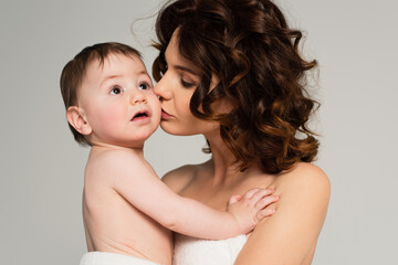 mother with bare shoulders kissing baby boy isolated on grey