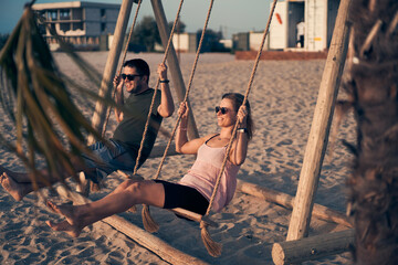 Young attractive couple swinging on seesaw on the beach.