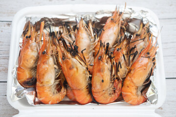 Thai grilled prawns in the shell placed foam box that wrap with foil paper.