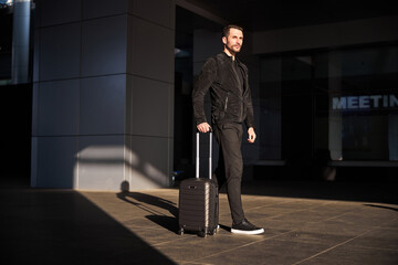 Confident traveler walking with his suitcase alone