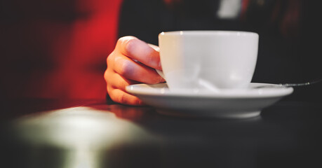 woman hands holding a white cup of tea or coffee standing on the table in cafe