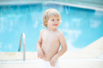 Happy child near swimming pool with blue water at summer
