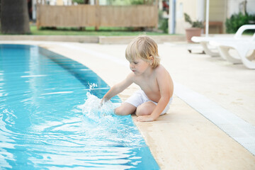 Happy child play near swimming pool with blue water at summer