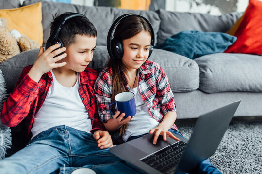 Portrait of brother and sister watching funny movie with headphones, while using laptop