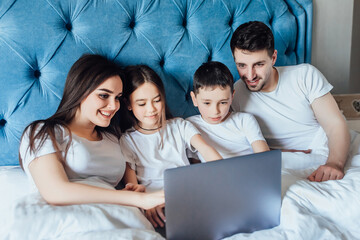 Happy family with kids lies on bed and watching something on laptop.Laughing and fun.