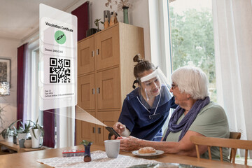 Home carer helping senior woman to use cell phone with Covid-19 vaccine certificate