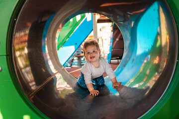 Funny caucasian baby girl playing on the playground, crawls in a tube. Outdoors. Concept of autism