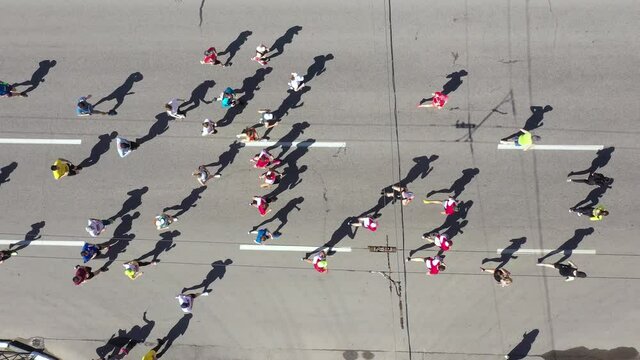 Aerial top down crowd of marathon contestants running in city, watcher standing on roadside and recording video, their shadows on asphalt road. Outdoor activity and healthy lifestyle. Concept of sport