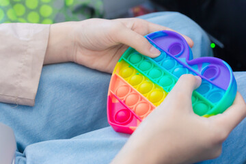 A toy of rainbow shades popit in the hands of a girl on the background of blue jeans. Concept of anemophobia: the fear of air.