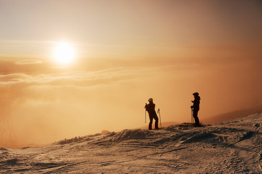 Skiers on snowy slope looking at sunset