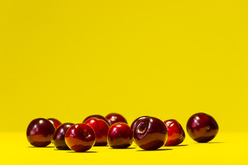 A horizontal summer bright yellow background with ripe cherries lying in a chaotic manner at the bottom of the photo.