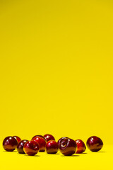 A bunch of ripe red cherries lies chaotically on a bright yellow summer background with plenty of space for insertion.