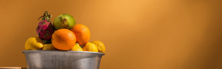 exotic fruits in metal bowl on orange background, banner