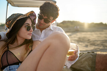 Young couple with sunglasses at sunset relaxing on a chaise longue, at sunset drinking wine and...